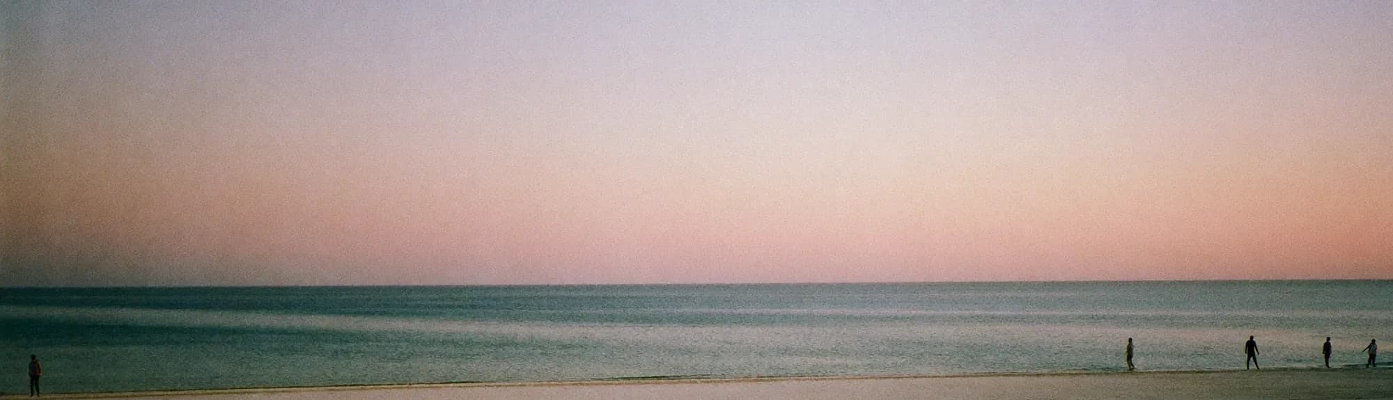The sea at dawn from a beach in Abu Dhabi, a few people at the water's edge.